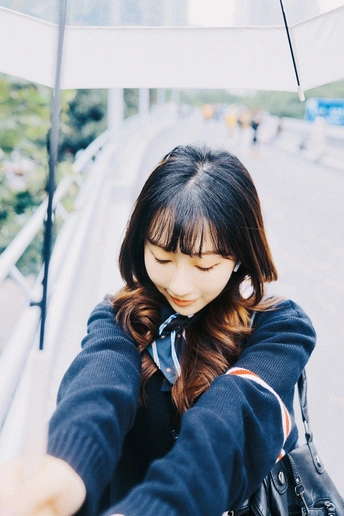 一位年轻女子手持白色雨伞 正看着手机