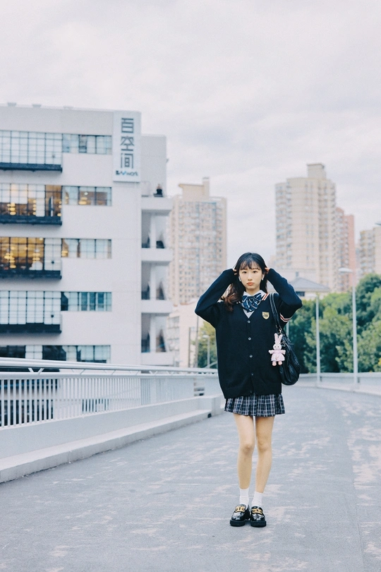 一个穿着黑色连衣裙和背包的年轻女孩站在桥上 背景是建筑物。