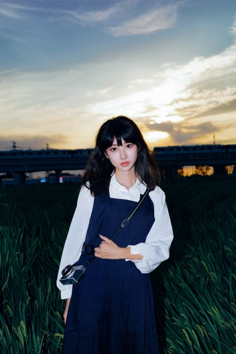 一个穿着蓝色连衣裙的年轻女子站在夕阳下的 tall grass 中。