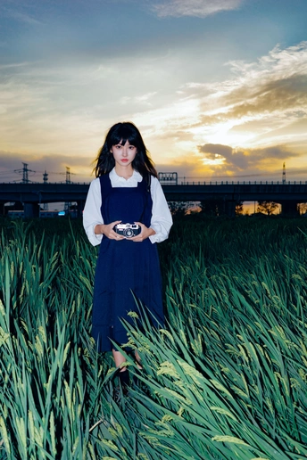 一个穿着蓝色连衣裙的年轻女子站在夕阳下的草地上