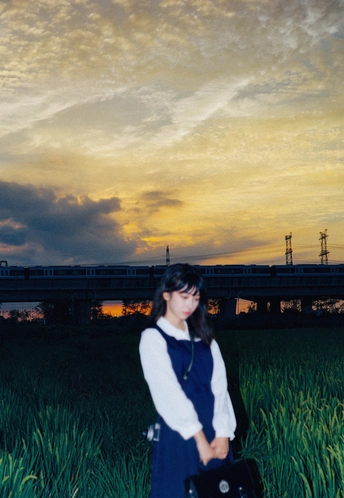 一个年轻女子站在夕阳下的草地上 手里拿着一个手提箱。