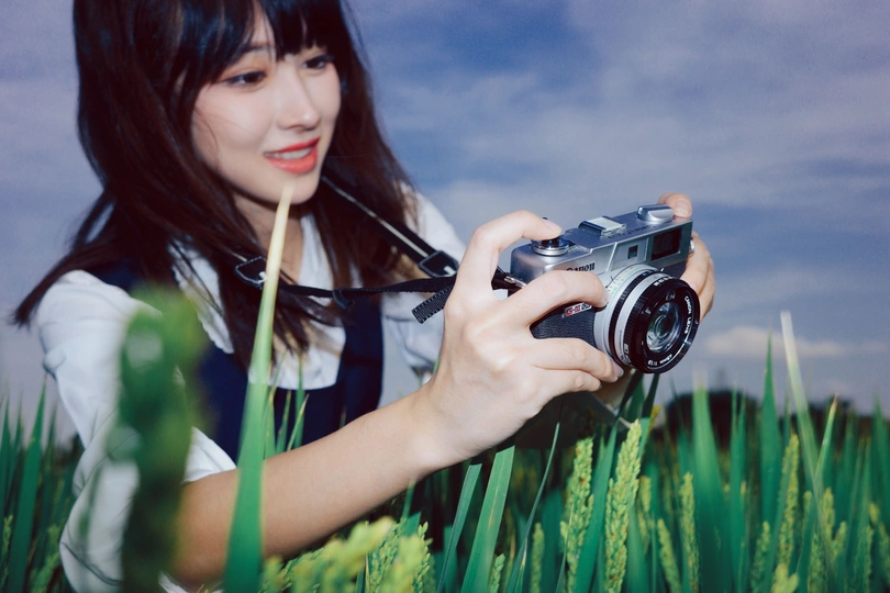 一位年轻女子手持相机在绿草地上拍照