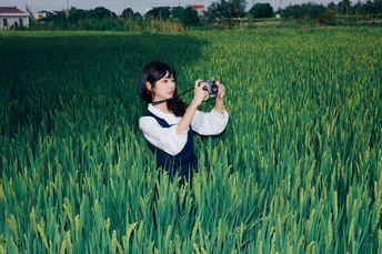 一位站在绿色麦田中的女性正在用她的相机拍照。