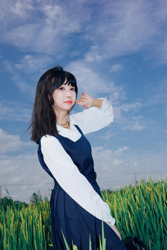 一位穿着白色连衣裙的年轻女子站在一片绿色的草地上