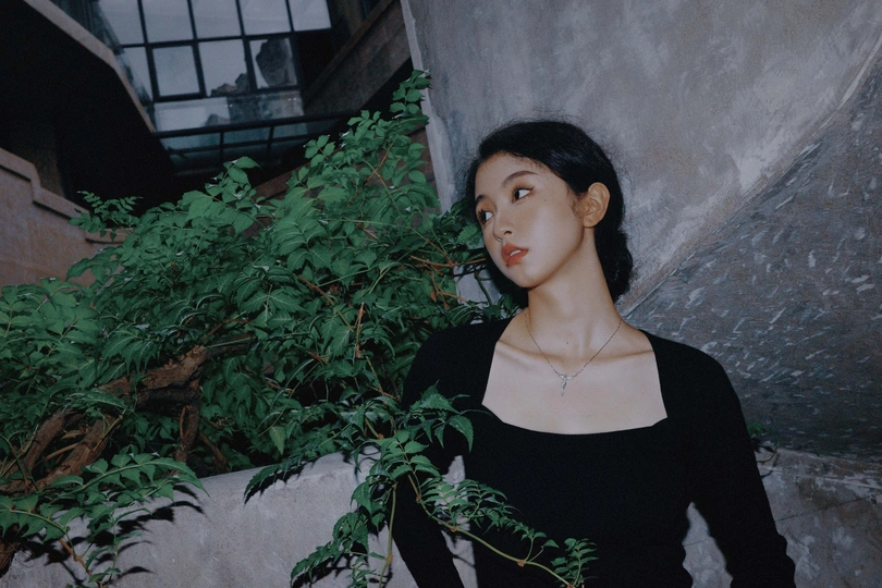 一位穿着黑色连衣裙的年轻女子站在一株植物旁边