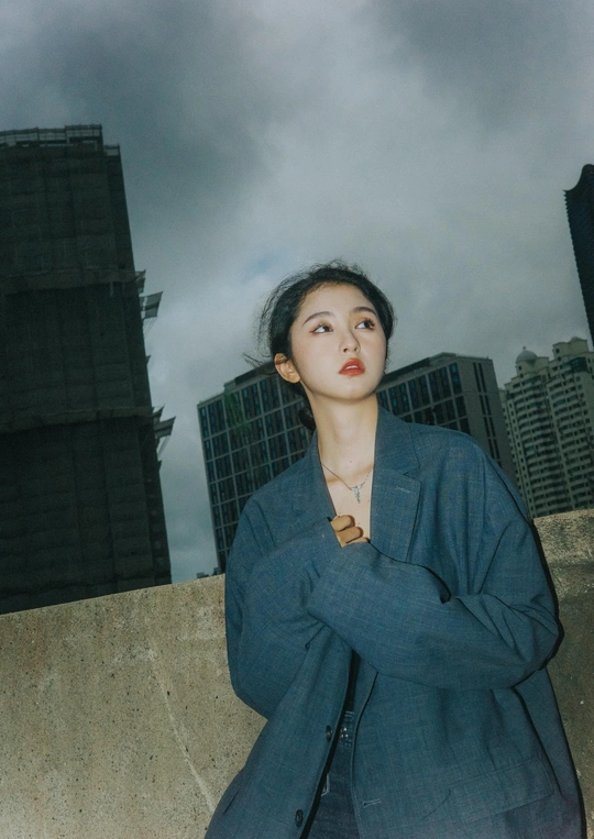 一位穿着蓝色西装的女性在背景中有建筑和天空的墙前摆姿势