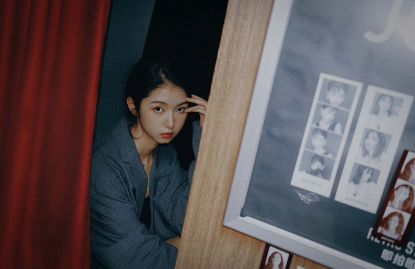 一位年轻女子靠在一扇门上 透过窗户上的窗帘向外看。