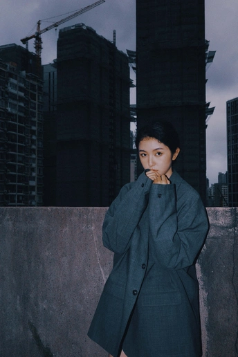 一位穿着西装和外套的女人站在一栋建筑的屋顶上 背景是一个城市。