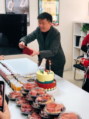 一个人正在蛋糕上插蜡烛 而一个人站在桌子后面拍照。