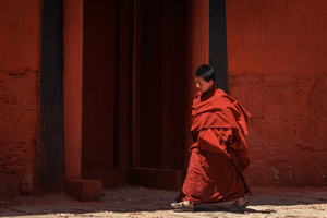 一位穿着红袍子的女人正在街上走 而一位穿着红袍子的男人则坐在红墙边。