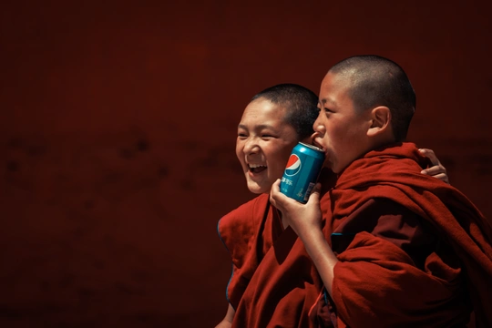 一个穿着僧袍的年轻男孩举着手机贴在耳边 一个男子站在他身后