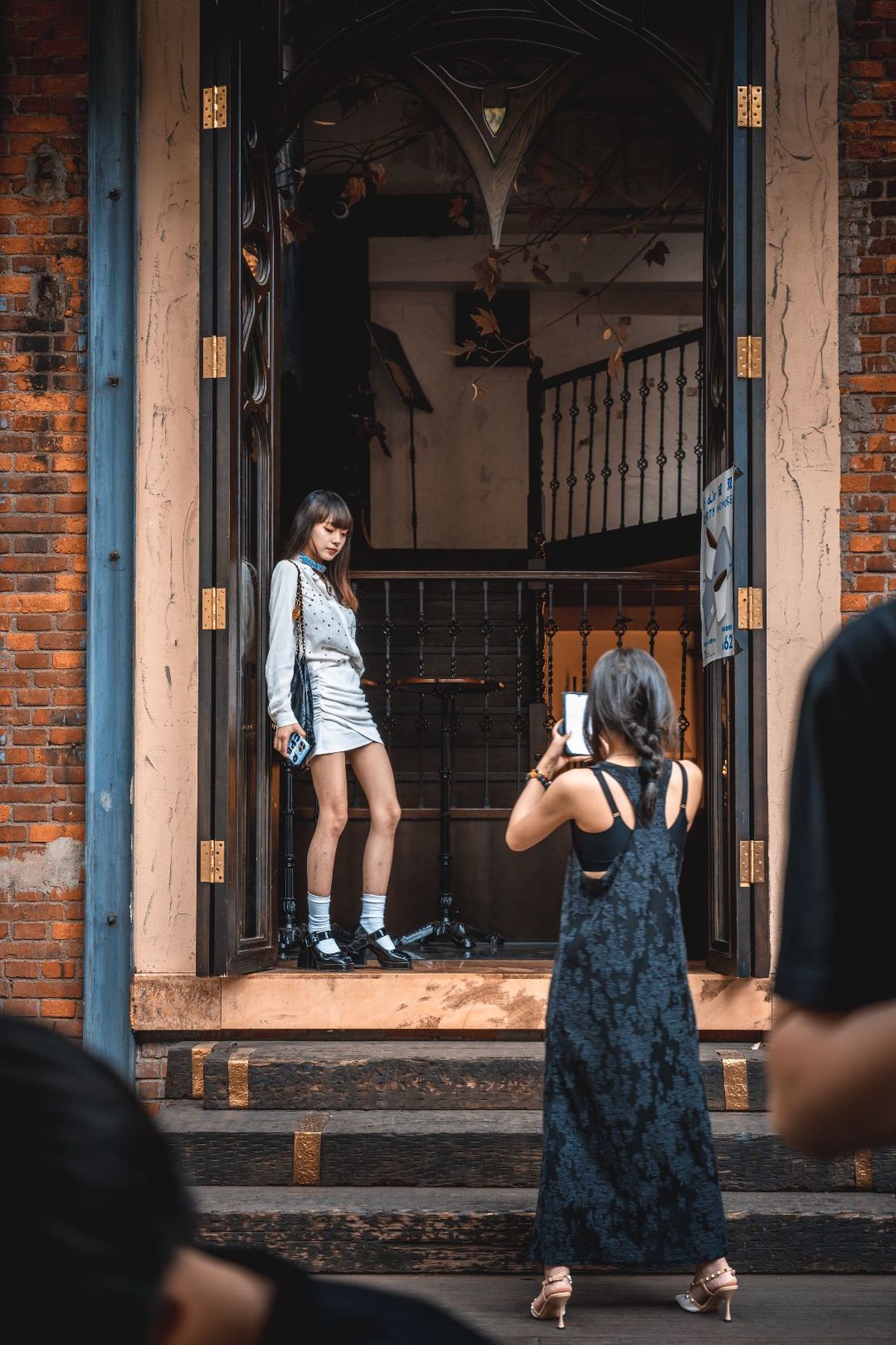 站在建筑物前穿着连衣裙的年轻女孩 人们正在拍照。