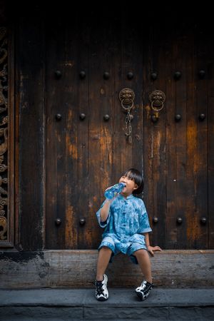 一个小女孩穿着蓝色裙子坐在木门前面
