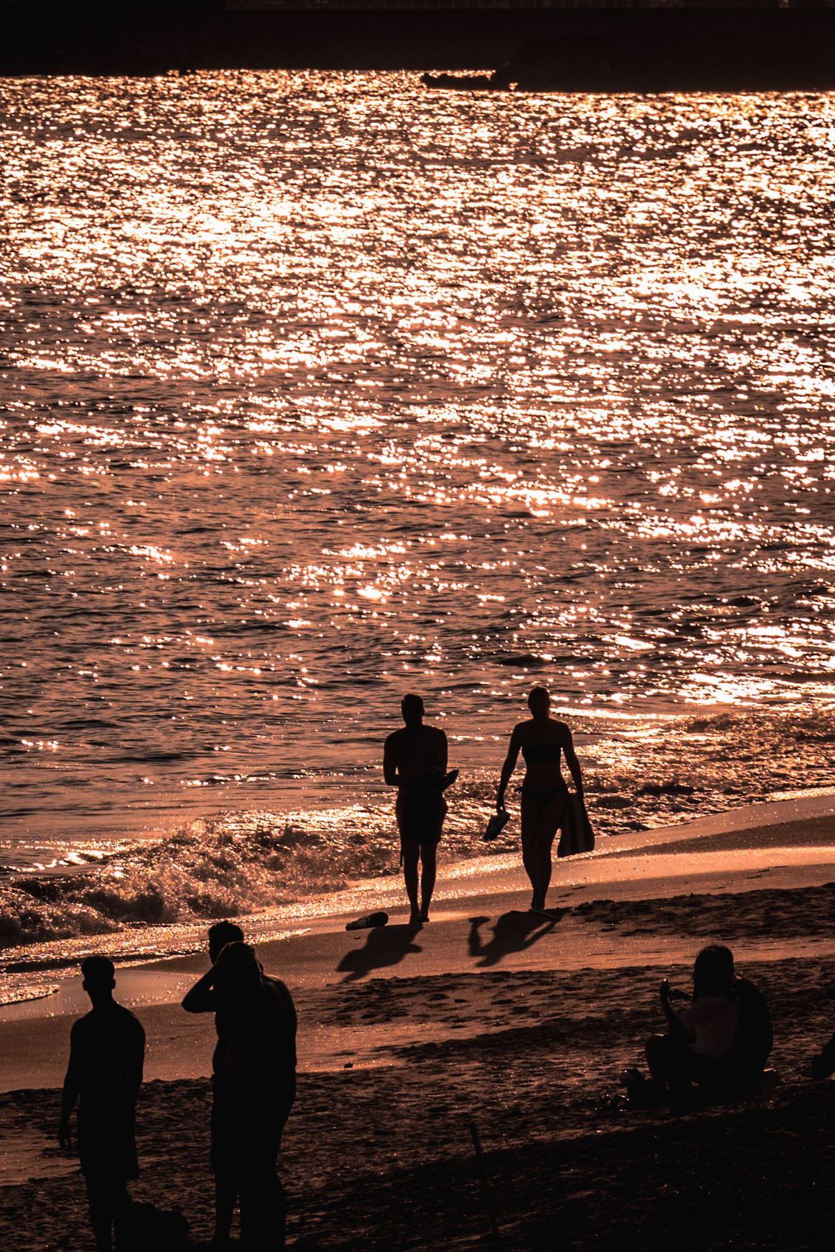 夕阳西下 几名带着冲浪板的游客沿着海滩走。