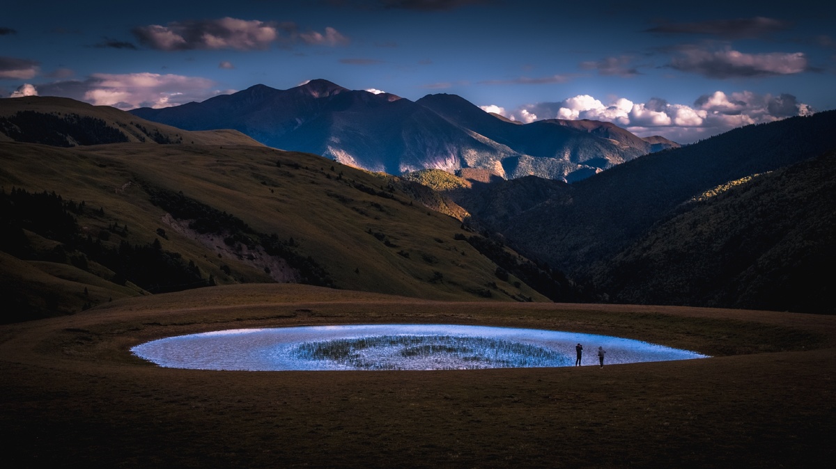 夜晚拍摄的一张照片 一对夫妇站在山谷中的一个湖前面 背景是山脉。