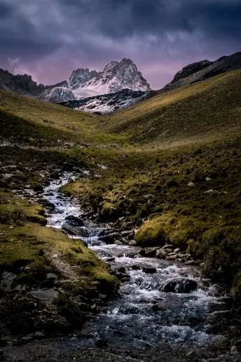 一个山谷 溪流穿过其中 背景是山脉 有戏剧性的天空。