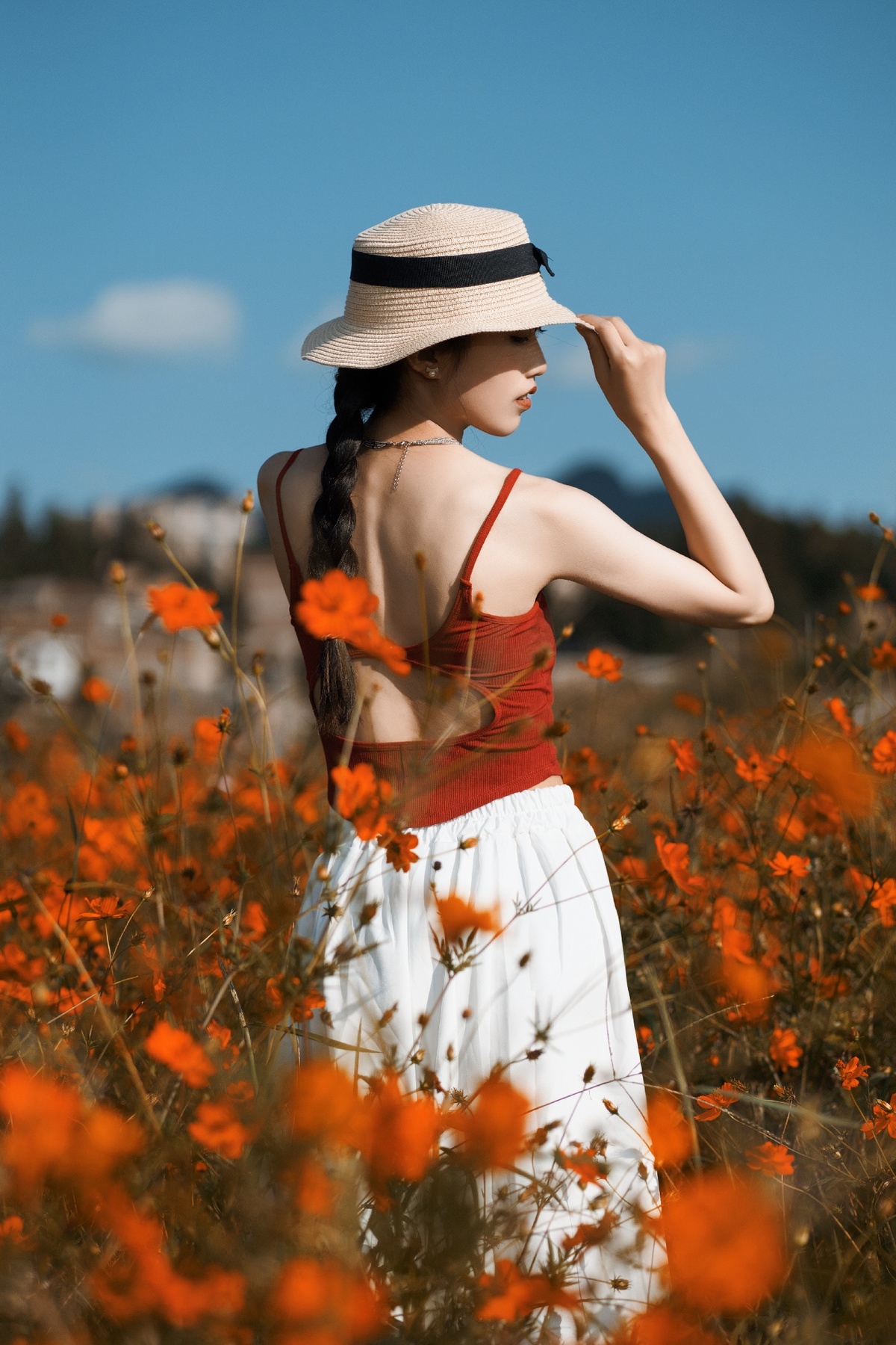一位穿着白色连衣裙和帽子站在橙花田中的年轻女子