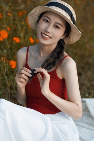 一位穿着红色连衣裙和帽子坐在白色花丛中的年轻女子