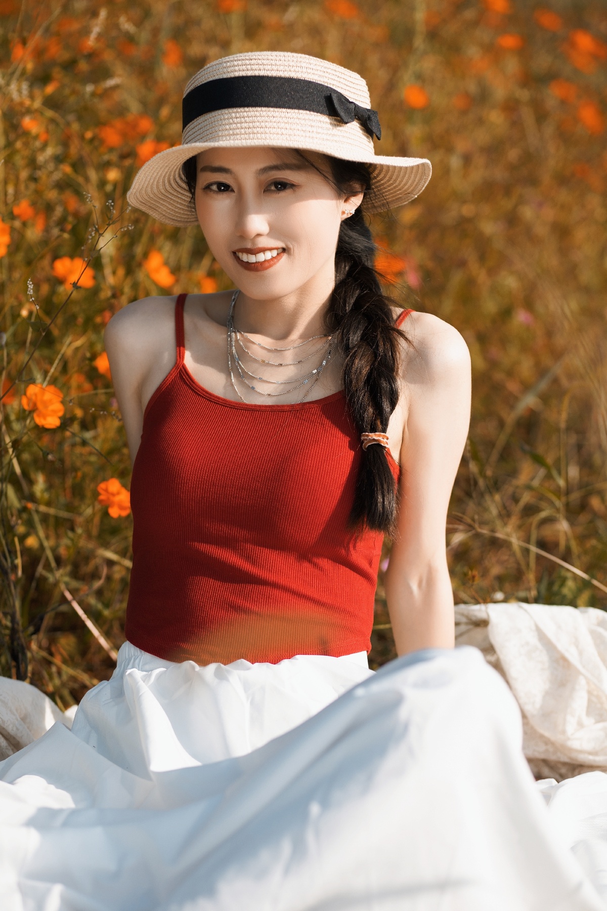 一位穿着红色连衣裙和白色帽子的年轻女子坐在花床垫上。