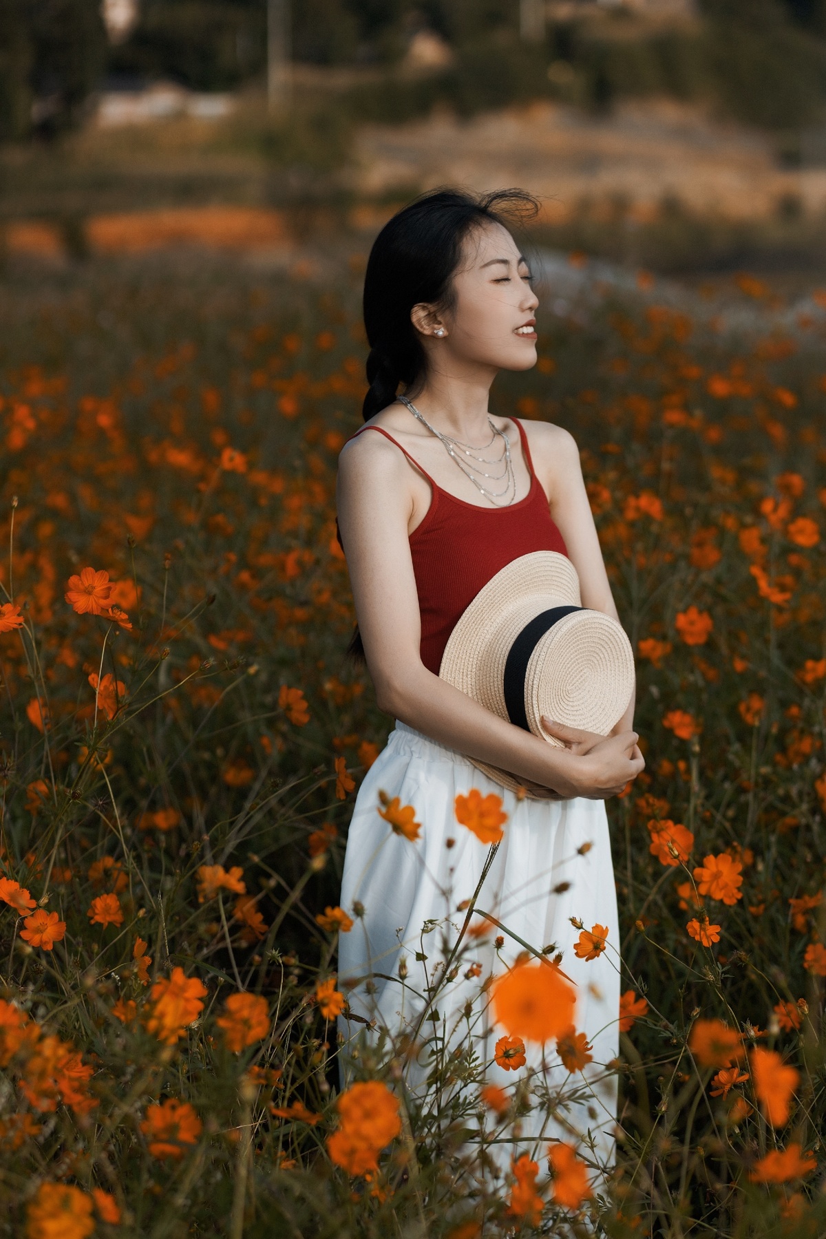 一位穿着白色连衣裙的年轻女子 戴着帽子 站在一片橙色花的田野中。
