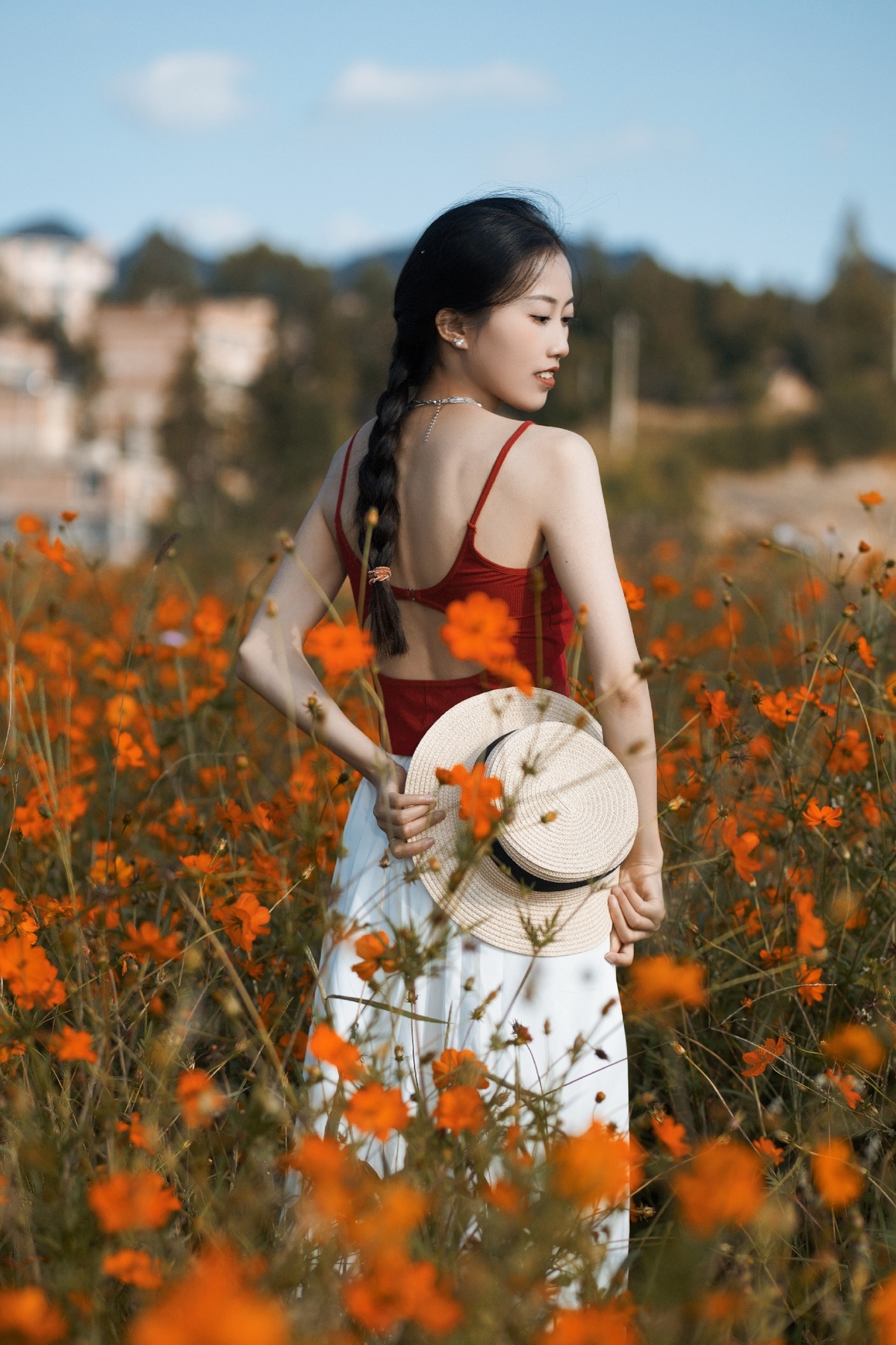一位穿着白色连衣裙和红色帽子的年轻女子穿过一个橙色田野