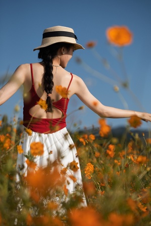 一位穿着红色连衣裙和帽子站在橙色花田中的年轻女子