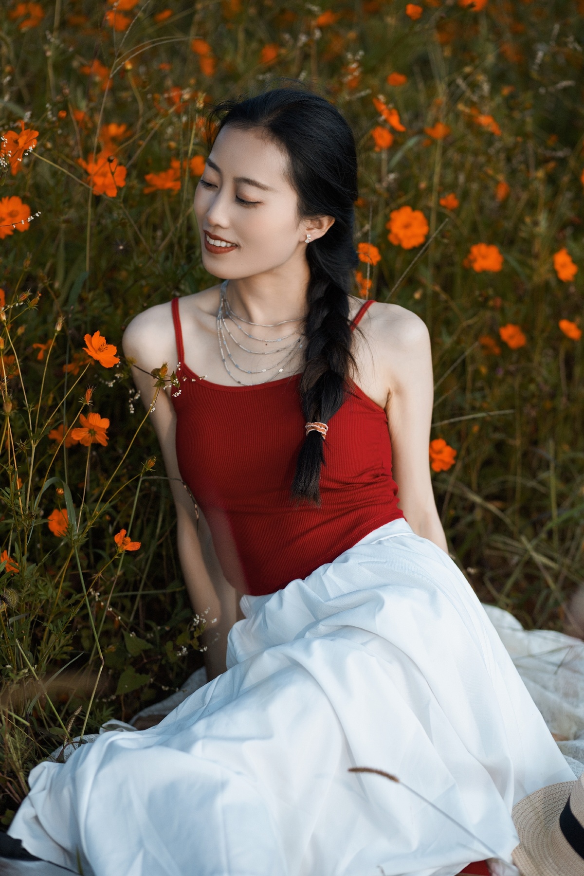 一位穿着红裙子的美丽年轻女子坐在橙花丛中