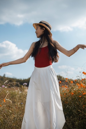 一位穿着白色连衣裙和红色帽子的年轻女子 站在开满鲜花的草地上 伸开双臂 仰望天空。