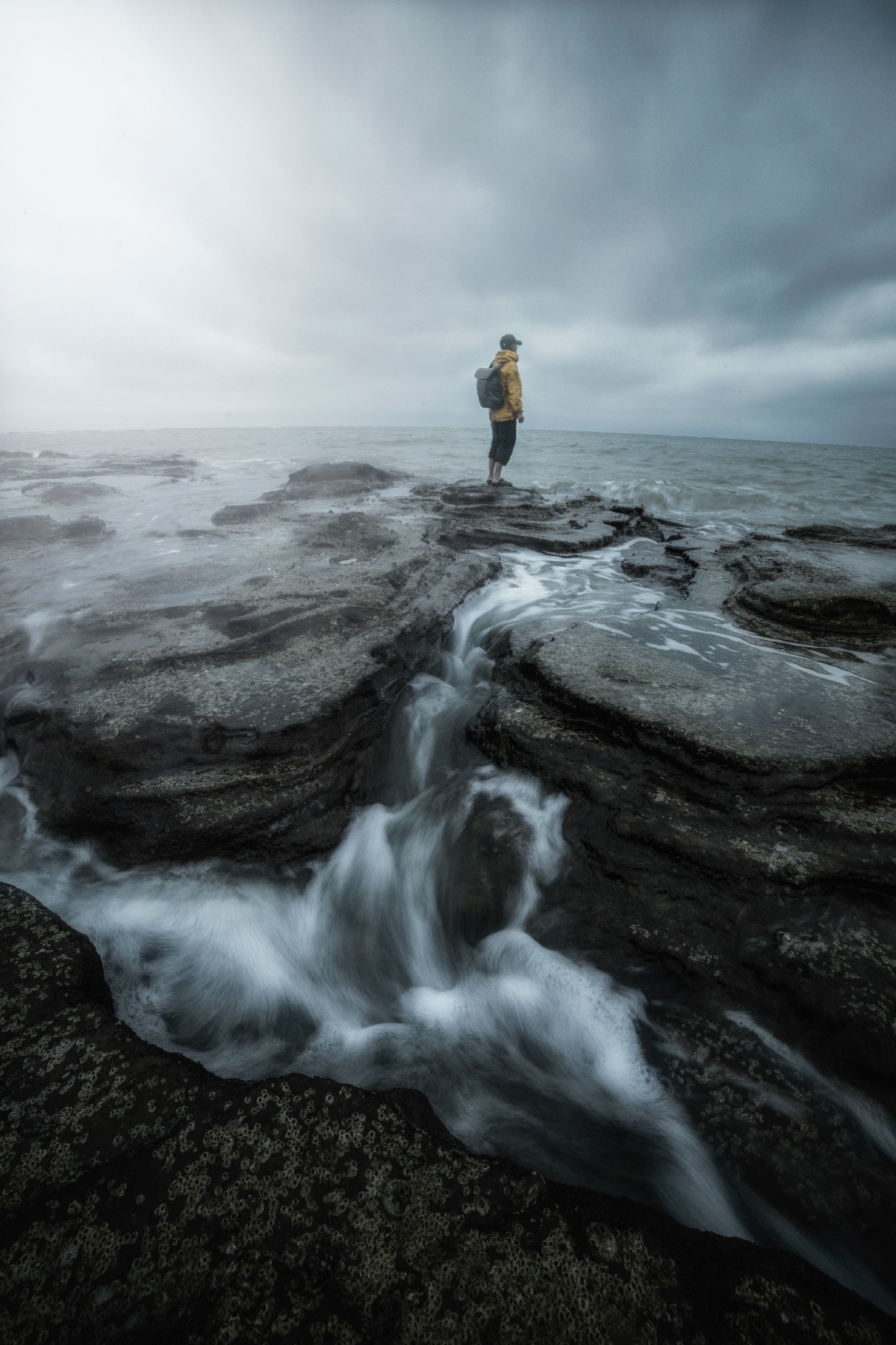 一个穿黄衣服的男子站在一块岩石上 眺望着大海。