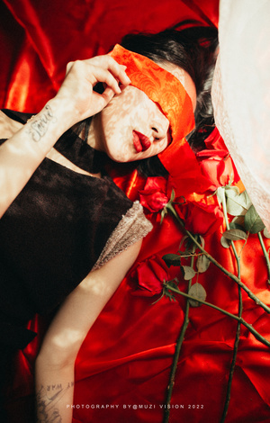 当一个男人躺在红玫瑰床上时 一个戴着黑橙色口罩的女人用手捂住眼睛