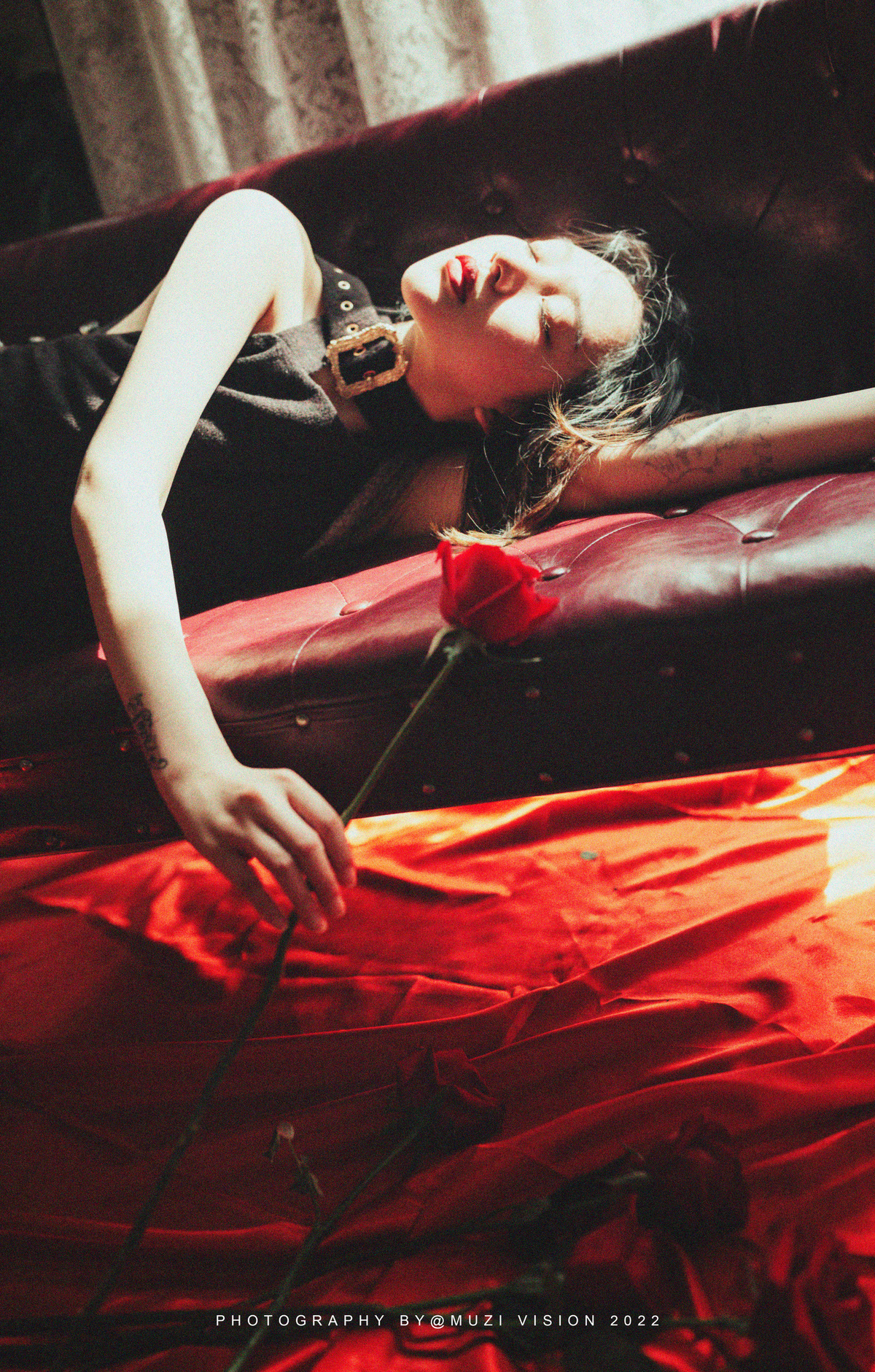一个穿着黑色连衣裙的年轻女人躺在红色沙发上 手里拿着一朵玫瑰