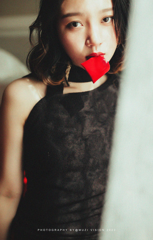 一位身穿黑色连衣裙的年轻女子拿着一面嘴唇上涂着红色口红的镜子