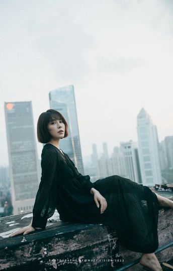 一个穿着黑色连衣裙的女人坐在俯瞰城市的屋顶上