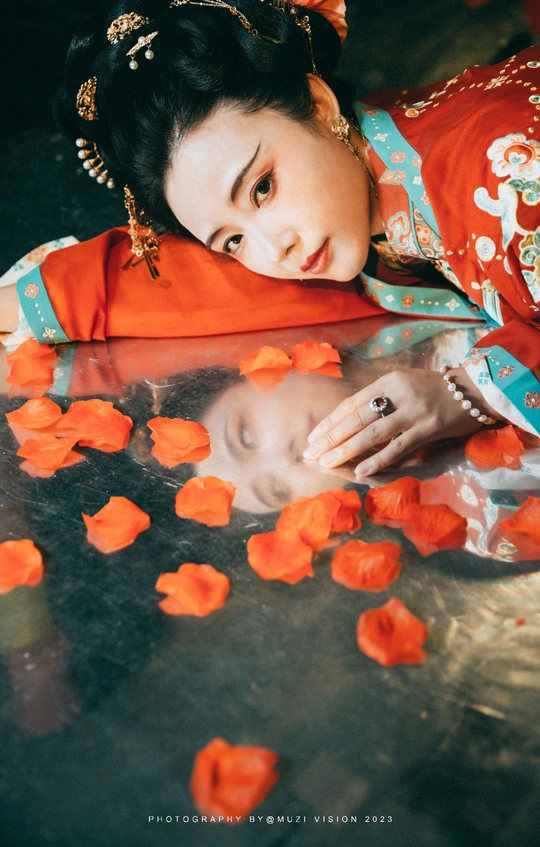 一位穿着红裙子的年轻女子 裙子上铺满了花瓣 地板上也有花瓣。