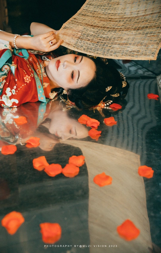 一个穿着连衣裙 裙子上铺着花瓣 手里拿着雨伞的女人 正躺在地上。