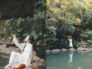 一个穿着白色连衣裙的女孩在池塘边岩石上拿着一把伞