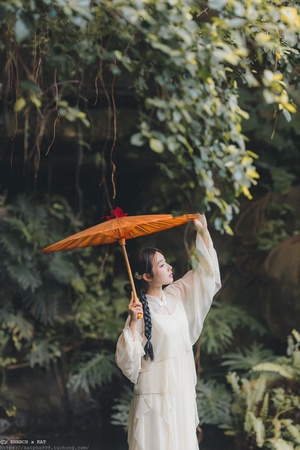 一位穿着白色连衣裙的女人举着一把橙色雨伞遮在她的头上