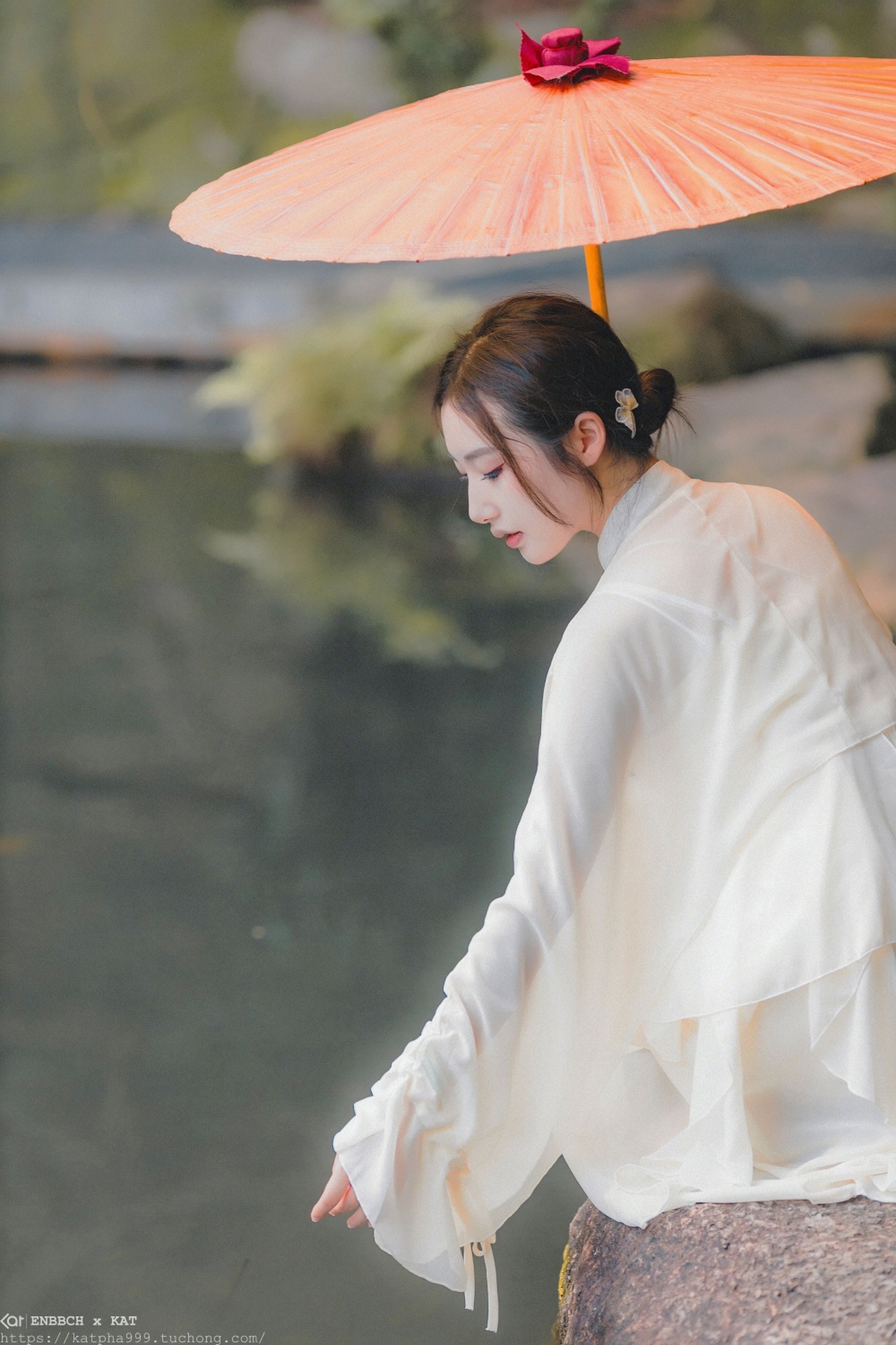 一位穿着白色和服的年轻女子手持雨伞站在水边