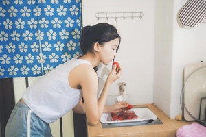 一位年轻女子站在厨房桌子旁吃草莓