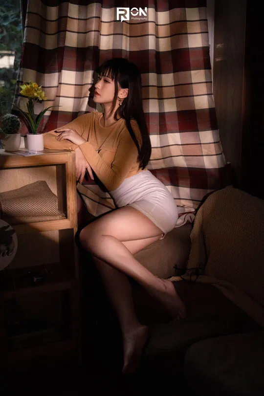 一个年轻女子坐在带窗户和桌子的房间里的一把椅子上