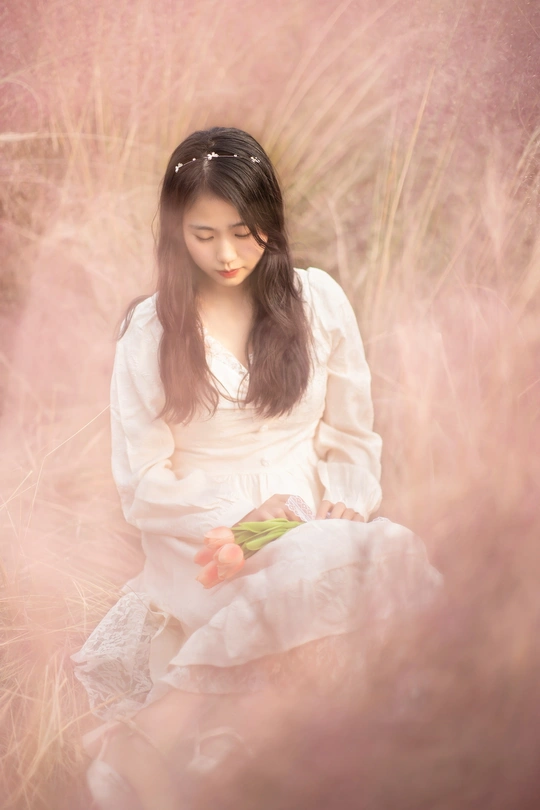 一位穿着白色连衣裙的年轻女子坐在粉红色花朵的田野中