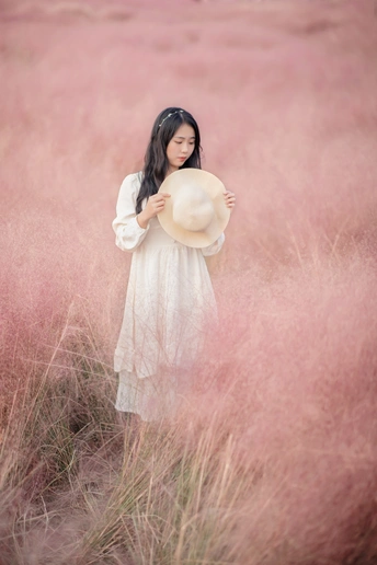 一位穿着白色连衣裙的年轻女子站在一片高草丛中。