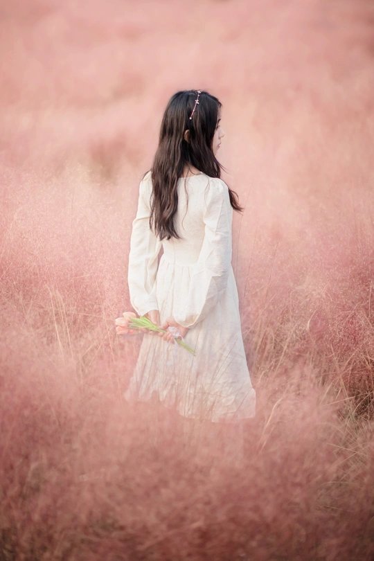 一个穿着白色连衣裙的年轻女子站在一片高草地里