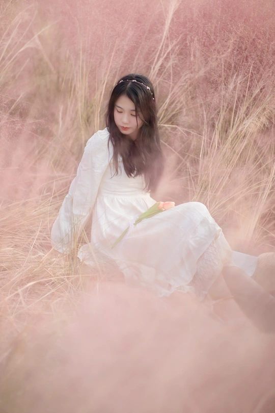 一个穿着白色连衣裙的年轻女子坐在一片高草地上