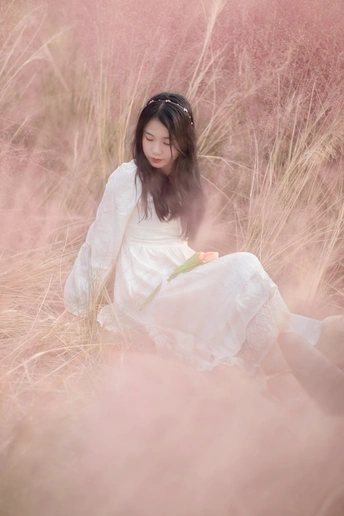 一个穿着白色连衣裙的年轻女子坐在一片高草地上