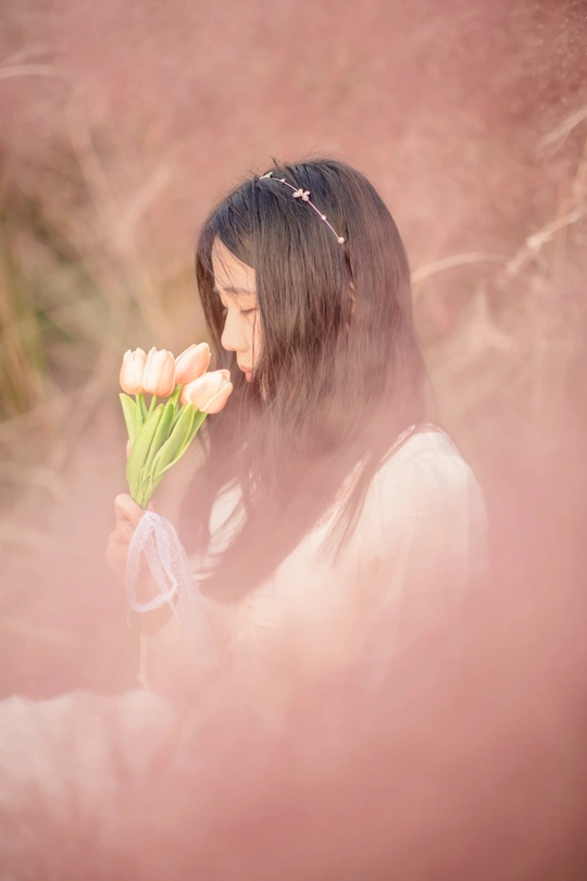 一位年轻女子手持白色郁金香 置身于粉色花丛中。