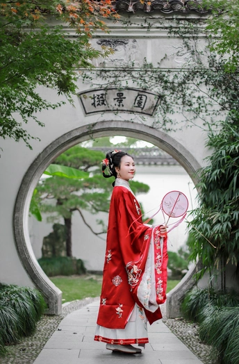 一位穿着传统红色裙子的年轻女子手持雨伞走过拱门。