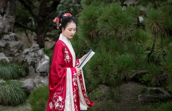 一位穿着日本传统红色和服的年轻女子在花园里读书。