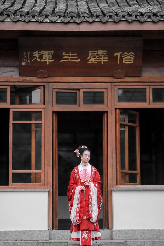 一位穿着红色连衣裙的年轻女子站在一栋建筑前