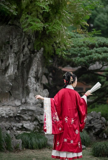 一位穿着传统红色和服的女性 手持雨伞站在花园里。